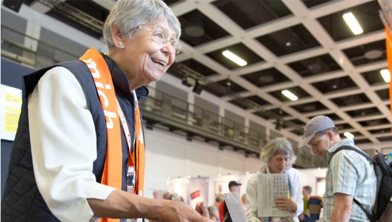 Teilnehmerin beim Kirchentag in Berlin 2017 (Foto: DEKT/Jenna Dallwitz) Eine Teilnehmerin im Zentrum Älterwerden streckt die Hand aus, sie trägt den orangenen Schal des Berliner Kirchentages und lacht