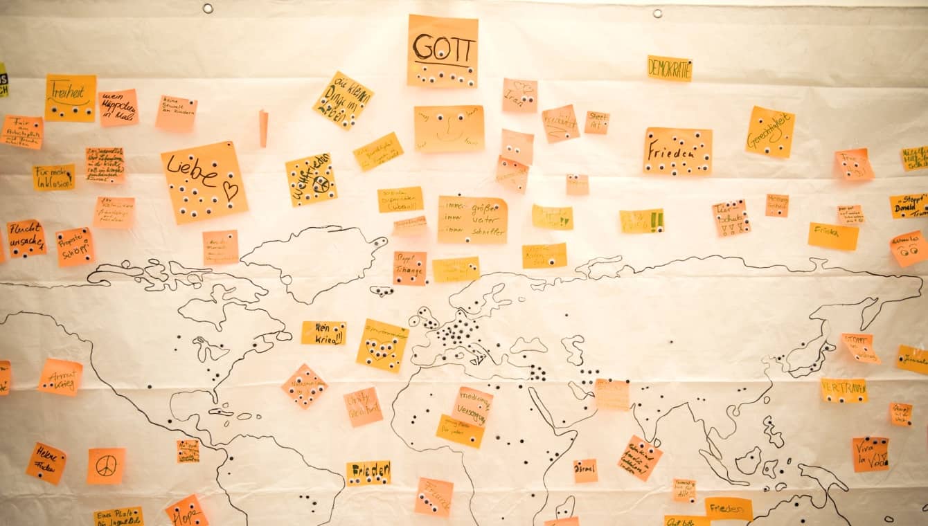 Klebezettel bei einem Workshop (Foto: Kirchentag/Jenna Dallwitz) Fragen nach Gott und der Welt - Collage aus orangenen Klebezetteln auf einer Weltkarte im Zentrum Jugend beim Kirchentag in Berlin - Wittenberg 2017